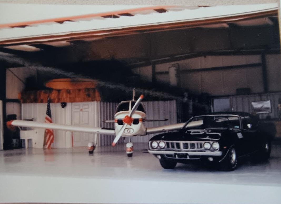 Dan Powell's hangar — his personal aircraft and black Plymouth 'Cuda parked side by side, two passions sharing the same roof