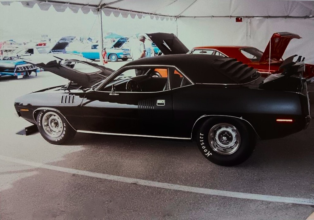 The Black Beast — Don Almeido's TX9 double-black 1971 426 Hemi Cuda on display at Mopars at the Strip, hood up, surrounded by other muscle cars under the show tent, 2003-2007 era